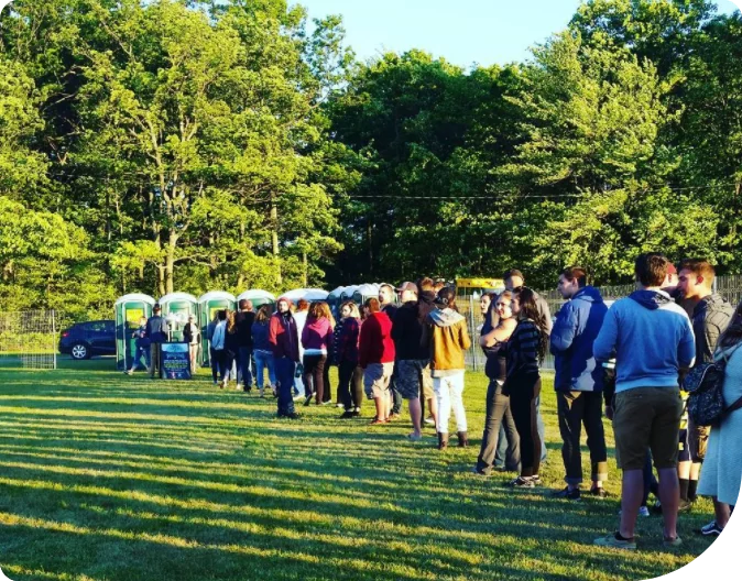 a line of people waiting to use outdoor porta potties